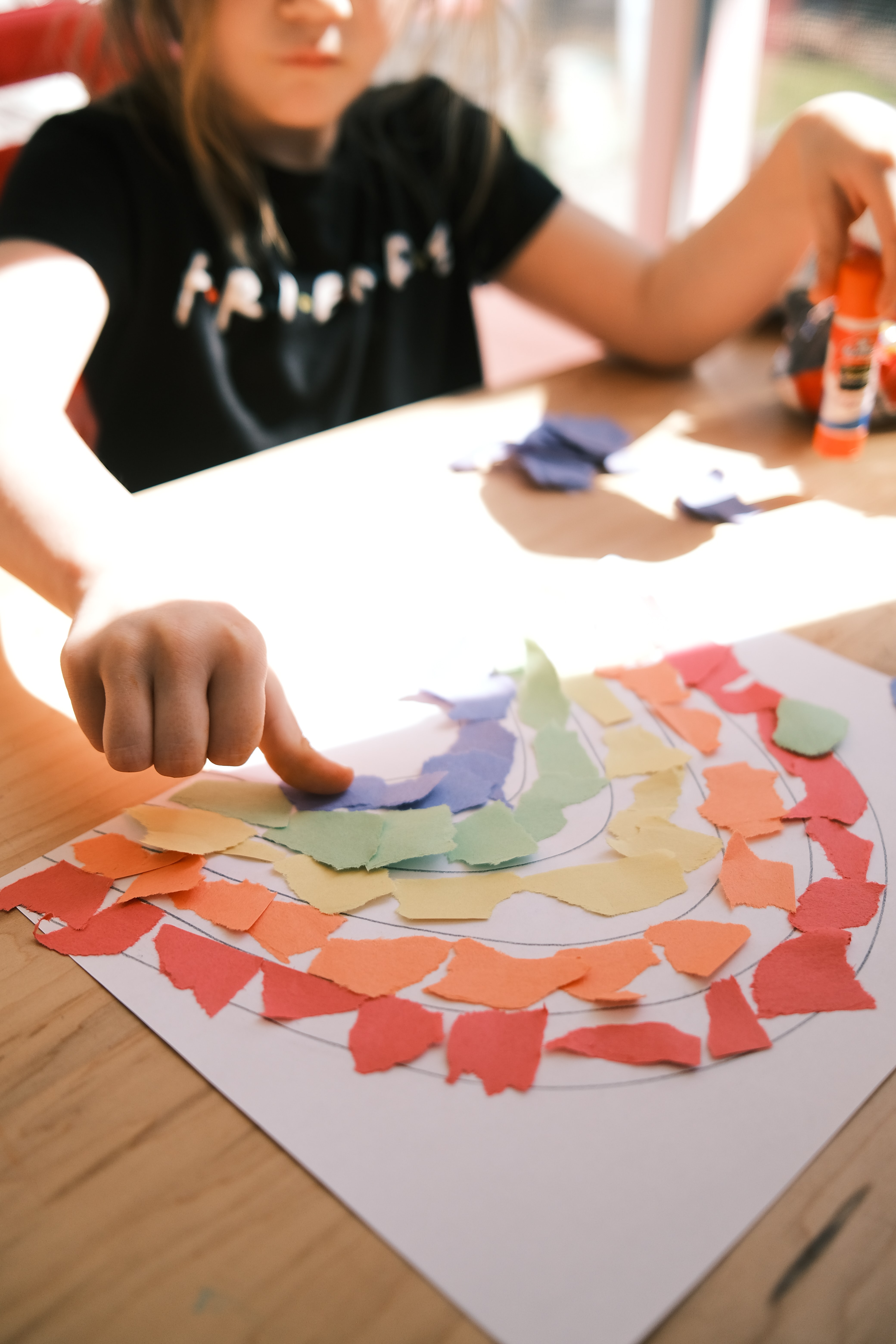 Child arranging torn pieces of colored construction paper on rainbow