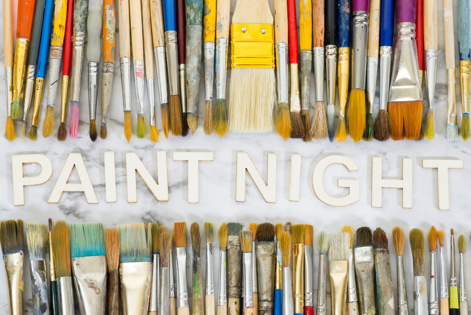 Rows of paintbrushes with wooden letters spelling "Paint Night"