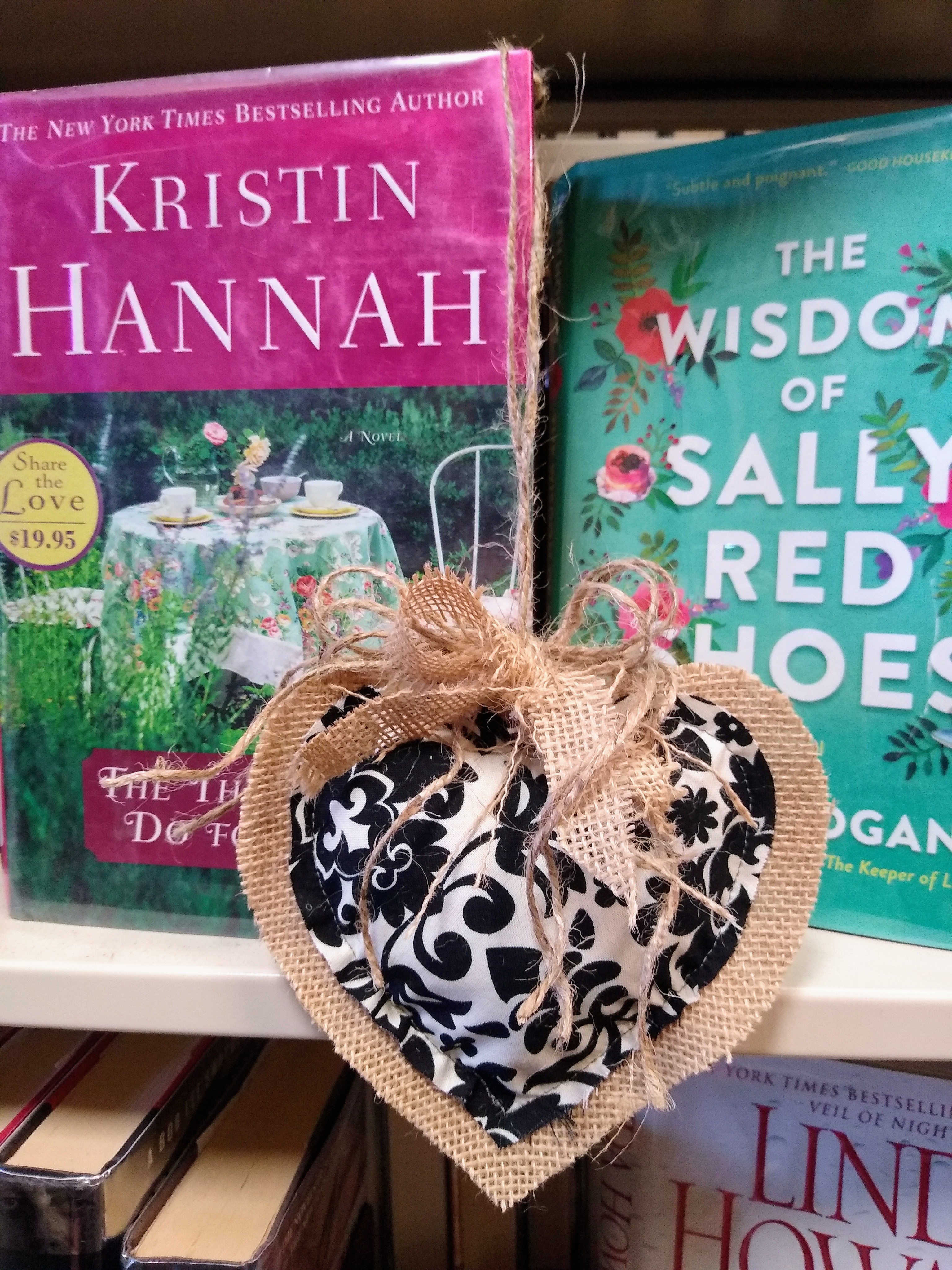 Burlap heart with a black and white fabric pattern on the front, hanging on a book shelf with two books in the background.
