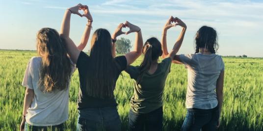Teens in a field making heart shapes with their hands