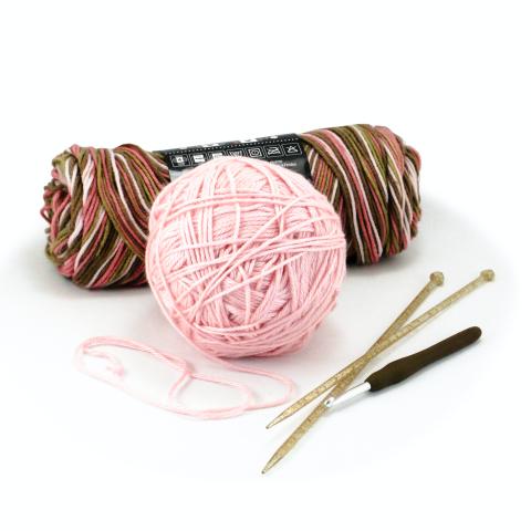 Skein of multicolored yarn and ball of pink yarn with knitting needles and crochet hook