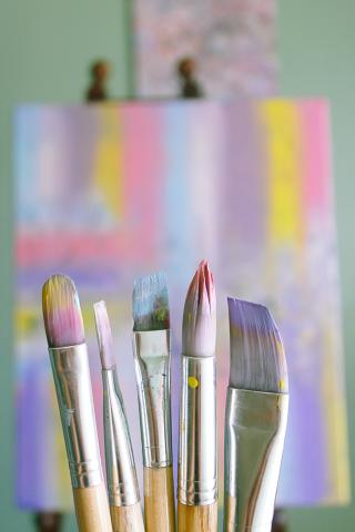 Pastel paint on paintbrushes with canvas in background